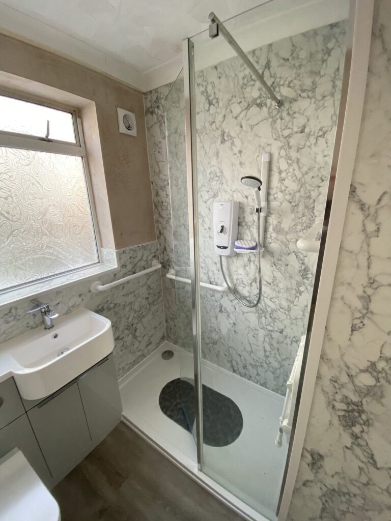 Accessible walk-in shower room with grab rails, marble-effect wall panels and vanity unit, fitted by CMG Heating & Plumbing