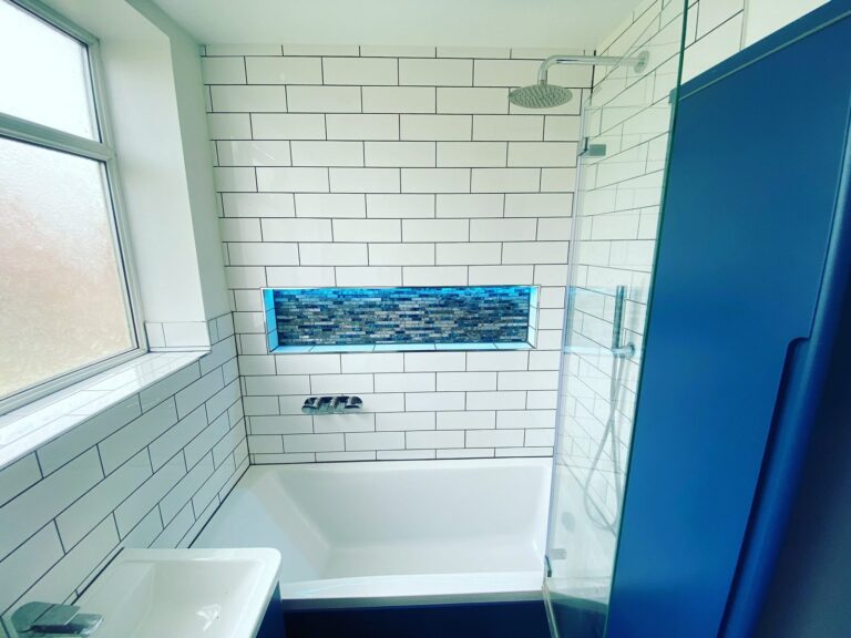Bathroom with white metro tiling, illuminated mosaic niche and bath shower screen